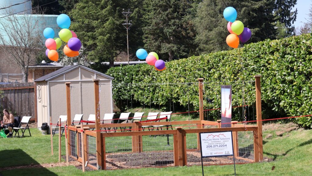 Vista del jardín comunitario de Mercy House con camas de cultivo y decoración durante el evento de inauguración