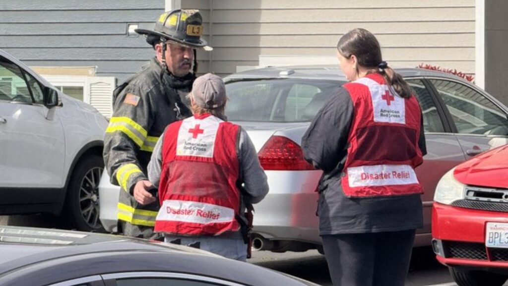 Personal del Departamento de Bomberos de Tacoma conversa con voluntarias de la Cruz Roja Americana frente a un complejo de apartamentos tras un incendio que dejó una persona fallecida y varios residentes evacuados.