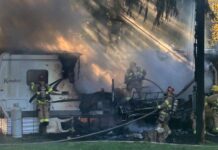 Dos personas mueren en incendio de un tráiler en Woodinville Bomberos combaten un incendio activo en un tráiler en Woodinville, rodeado de humo espeso y llamas visibles, mientras trabajan cerca de un tanque de propano y postes eléctricos.