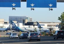 Alaska Airlines aumenta sus tarifas de equipaje en 2026 Carretera de acceso al Aeropuerto Internacional de Seattle-Tacoma (SEA). Aeronaves de Alaska Airlines permanecen en pista al fondo — Imagen: Latino Herald ™