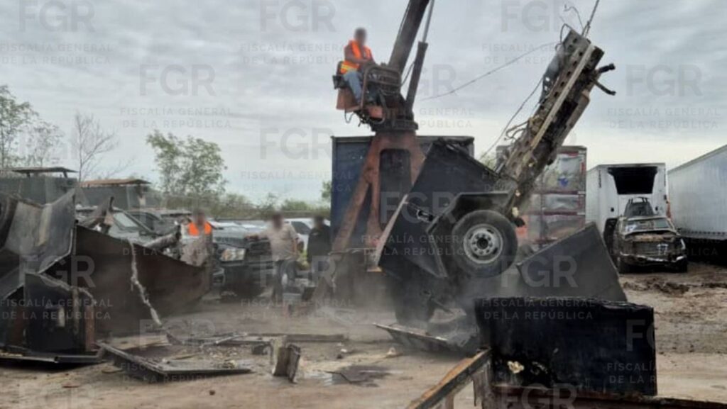 Maquinaria pesada destruye un vehículo blindado artesanal mientras trabajadores con chalecos de seguridad supervisan el proceso en un terreno abierto; alrededor se observan restos metálicos y otras unidades dañadas, en un operativo de autoridades federales en México.