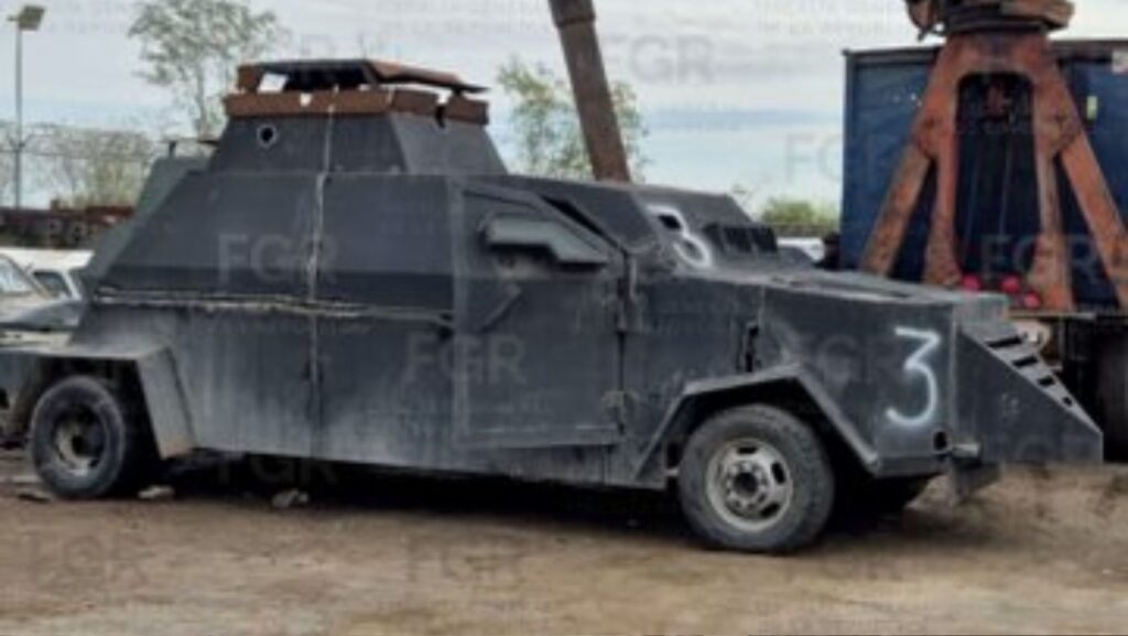Vehículo blindado artesanal tipo “monstruo” de color oscuro, con placas metálicas gruesas y estructura reforzada, estacionado en un terreno abierto mientras maquinaria pesada se prepara para su destrucción en un operativo federal en México.