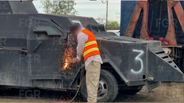 Un trabajador participa en la destrucción de un vehículo blindado Trabajador con chaleco de seguridad corta con soplete la estructura metálica de un vehículo blindado artesanal tipo “monstruo”, generando chispas mientras forma parte de un operativo de destrucción en México.