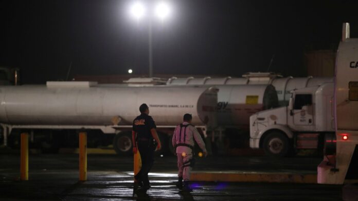 Un agente de la Policía Federal y un guardia de seguridad caminan cerca de camiones cisterna en un centro de almacenamiento y distribución de combustible de Petróleos Mexicanos. (Foto AP/Félix Márquez)