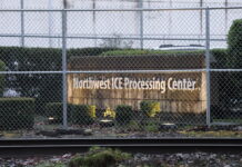 Juez autoriza inspecciones sanitarias en el centro de detención de GEO en Tacoma Vista exterior del Northwest ICE Processing Center en Tacoma, Washington, detrás de una cerca de seguridad con alambre; se observa el letrero de la instalación y vías de tren en primer plano.