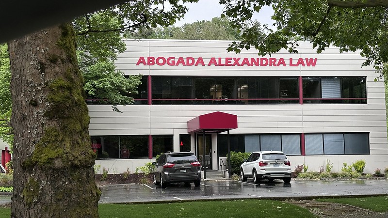 Exterior de edificio comercial con el letrero “ABOGADA ALEXANDRA LAW” en la fachada principal. La fotografía muestra el frente de las oficinas ubicadas en Tukwila, Washington, con vehículos estacionados frente al edificio. Foto: Latino Herald TM.