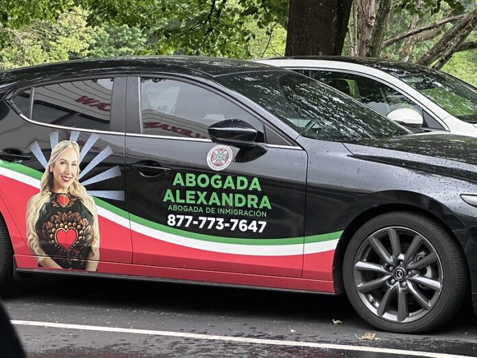 utomóvil negro con publicidad de “Abogada Alexandra” estacionado frente a oficinas ubicadas en 6720 Fort Dent Way Suite 230 en Tukwila, Washington. El vehículo muestra una imagen promocional de Alexandra Lozano, el texto “Abogada de Inmigración” y un número telefónico. Foto: Latino Herald TM.