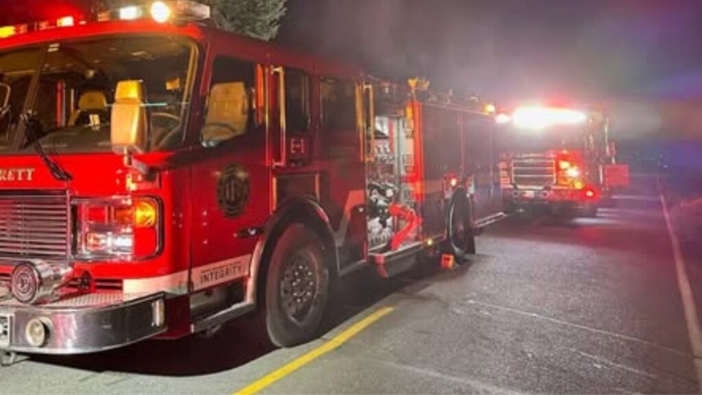 Camiones de bomberos de Everett estacionados en una calle durante la noche, con luces de emergencia encendidas y humo visible en el ambiente.