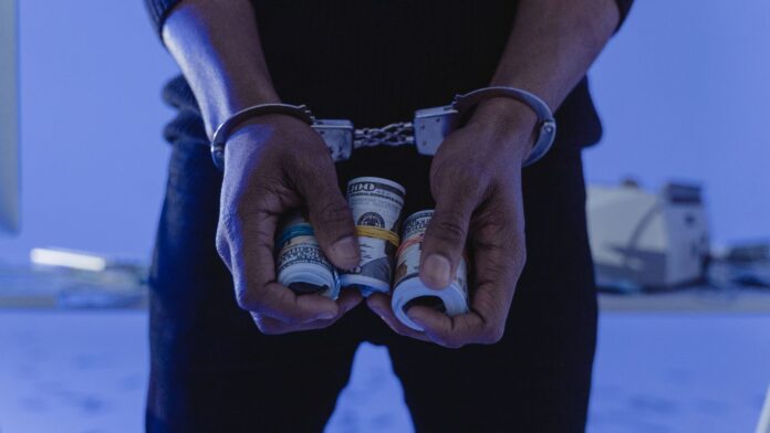 A Person with handcuffs Holding a Sum of Rolled Cash