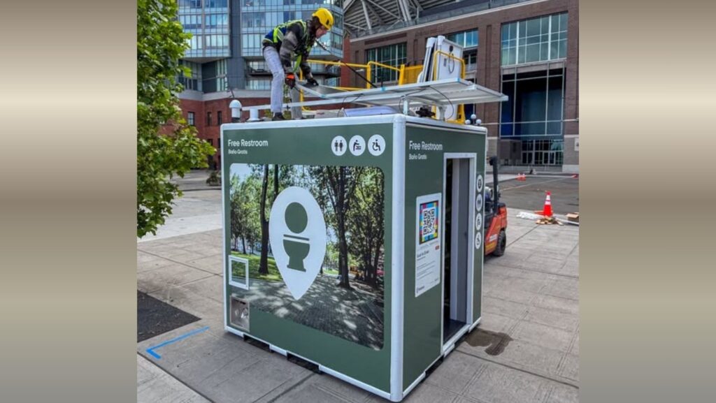 Un trabajador instala paneles solares sobre un módulo de baño público inteligente en Seattle. La estructura funciona con energía solar y cuenta con señalización de acceso gratuito y accesibilidad para personas con discapacidad.