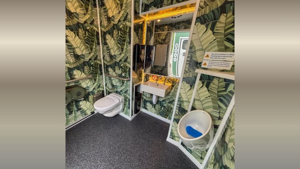 Interior de un baño público inteligente en Seattle con paredes decoradas con diseño tropical, inodoro, lavabo automático y sistema de limpieza integrado. La unidad funciona con tecnología automatizada y energía solar.