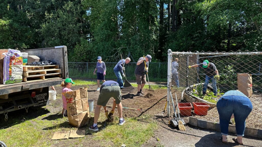 Voluntarios realizan labores de limpieza y mantenimiento en el jardín escolar de Scriber Lake High School durante una actividad comunitaria.
