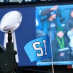 Seattle Seahawks acuerdan su venta por un récord de $9,600 millones al grupo de Vinod y Neal Khosla El trofeo Vince Lombardi y una bandera con el número 12 de los Seattle Seahawks durante la celebración del campeonato del Super Bowl en Lumen Field, en Seattle, en febrero de 2026. Al fondo se observan aficionados siguiendo el evento desde las gradas. Foto: Latino Herald™