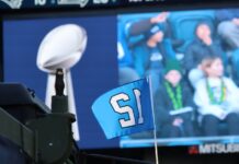 Seattle Seahawks acuerdan su venta por un récord de $9,600 millones al grupo de Vinod y Neal Khosla El trofeo Vince Lombardi y una bandera con el número 12 de los Seattle Seahawks durante la celebración del campeonato del Super Bowl en Lumen Field, en Seattle, en febrero de 2026. Al fondo se observan aficionados siguiendo el evento desde las gradas. Foto: Latino Herald™
