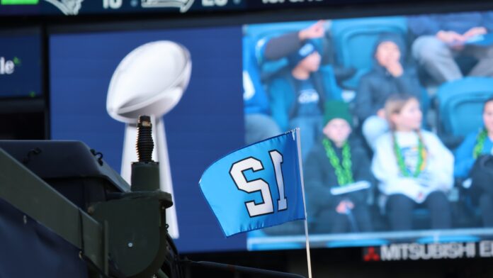 El trofeo Vince Lombardi y una bandera con el número 12 de los Seattle Seahawks durante la celebración del campeonato del Super Bowl en Lumen Field, en Seattle, en febrero de 2026. Al fondo se observan aficionados siguiendo el evento desde las gradas. Foto: Latino Herald™