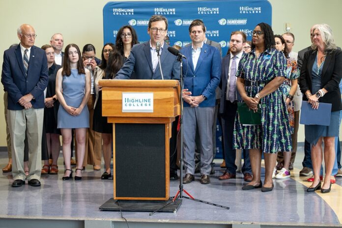 13 de julio de 2026. El gobernador Bob Ferguson habla desde un podio durante una conferencia de prensa en Highline College, en Des Moines, acompañado por estudiantes, funcionarios y representantes educativos, al anunciar una propuesta para exigir la FAFSA o la WASFA como requisito de graduación en Washington.