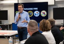 Incendio amenaza el agua de 35.000 personas en Walla Walla Bob Ferguson habla con un micrófono ante personal de emergencia, junto a un mapa y una pantalla con el nombre del incendio Paradise.