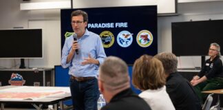 Incendio amenaza el agua de 35.000 personas en Walla Walla Bob Ferguson habla con un micrófono ante personal de emergencia, junto a un mapa y una pantalla con el nombre del incendio Paradise.