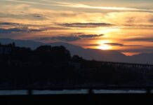 Julio rompe récord de calor en Estados Unidos mientras el humo amenaza regresar al Puget Sound Alt text: Atardecer sobre Seattle con el sol ocultándose detrás de las montañas Olímpicas, mientras una capa de neblina cubre parcialmente el horizonte del área de Puget Sound.