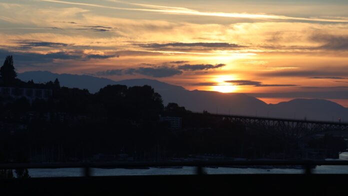 Atardecer en Seattle Alt text: Atardecer sobre Seattle con el sol ocultándose detrás de las montañas Olímpicas, mientras una capa de neblina cubre parcialmente el horizonte del área de Puget Sound.