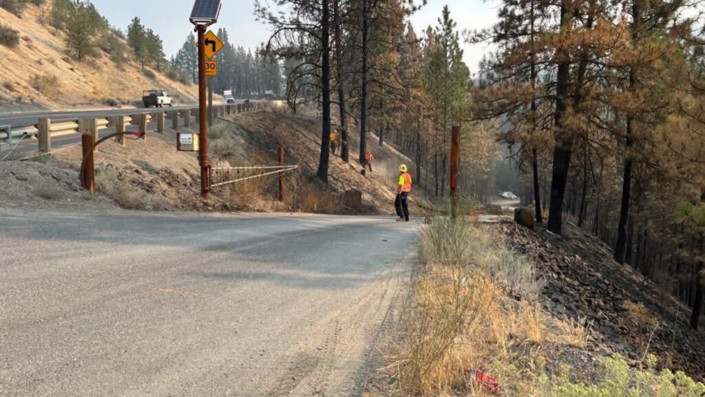 Trabajador realiza labores de recuperación junto a la SR 291 tras los incendios del complejo de Spokane.