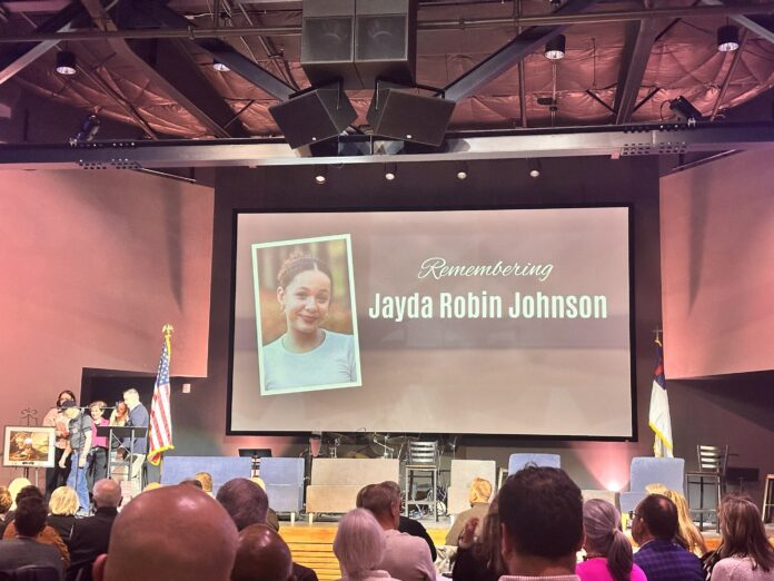 Fotografía tomada desde los asientos del público durante la gala de la organización sin fines de lucro Support 7, celebrada el 12 de abril de 2025 en Lynnwood. En el escenario, una pantalla gigante proyecta el retrato de Jayda Robin Johnson con el texto "Remembering Jayda Robin Johnson", mientras varios asistentes y presentadores permanecen en el estrado.