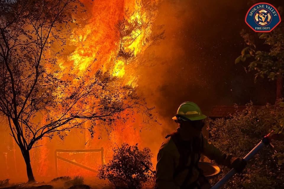 Un bombero combate intensas llamas que consumen árboles y vegetación durante un incendio forestal nocturno en el condado de Spokane.