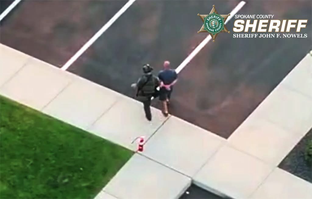 Un agente táctico escolta a un hombre esposado durante el operativo de arresto relacionado con la investigación del incendio Old Trails en el condado de Spokane.