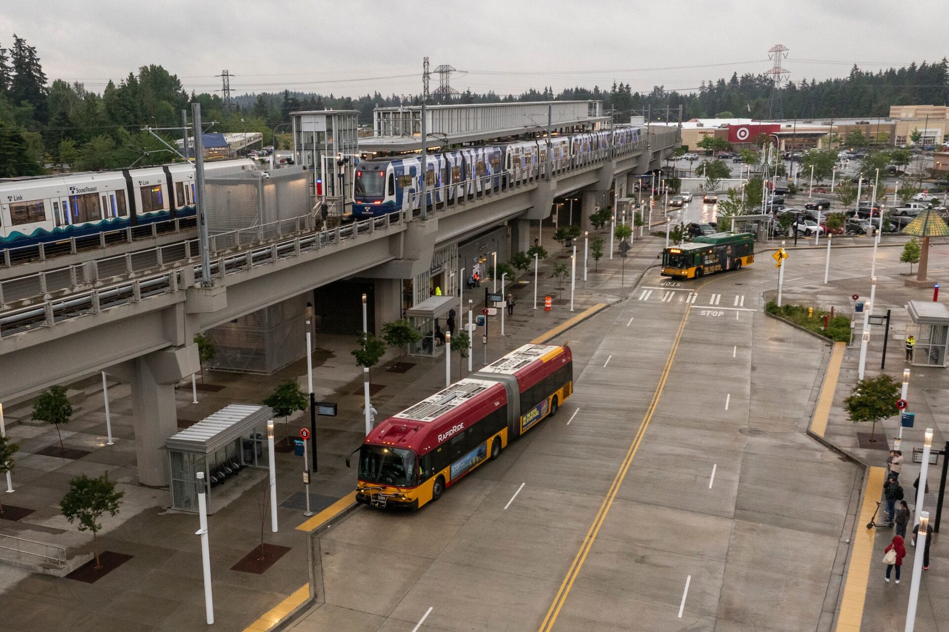 Vista del Federal Way Transit Center con trenes Link de Sound Transit en la vía elevada y autobuses de King County Metro circulando y estacionados en el centro de tránsito.