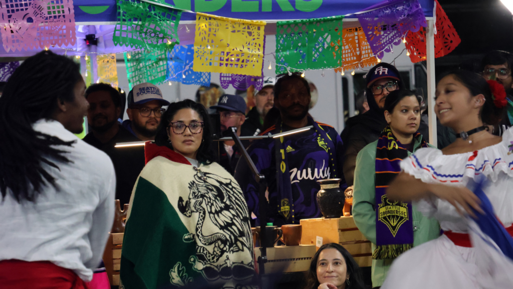 Bailarines de Caña Dulce se presentan rodeados por una multitud y puestos de vendedores durante Aquí Mercado, cerca de Lumen Field en Seattle.