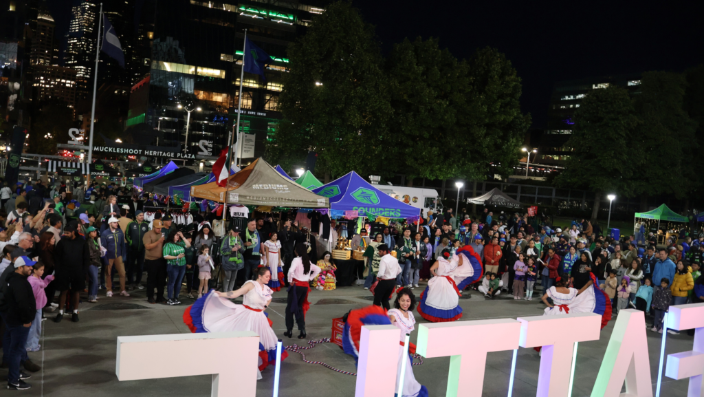 Integrantes de Caña Dulce bailan frente al público bajo decoraciones de papel picado durante Aquí Mercado, en Seattle.