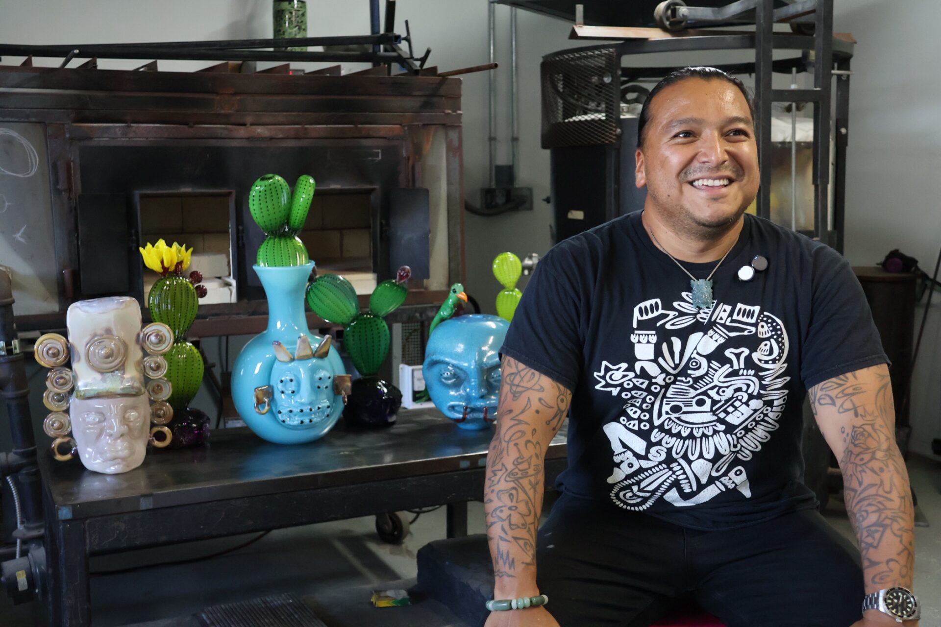 El artista mexicano Manolo Aguilera posa en su taller de vidrio en Everett, Washington, acompañado por varias de sus obras.