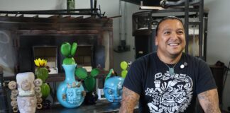 El artista mexicano Manolo Aguilera posa en su taller de vidrio en Everett, Washington, acompañado por varias de sus obras.