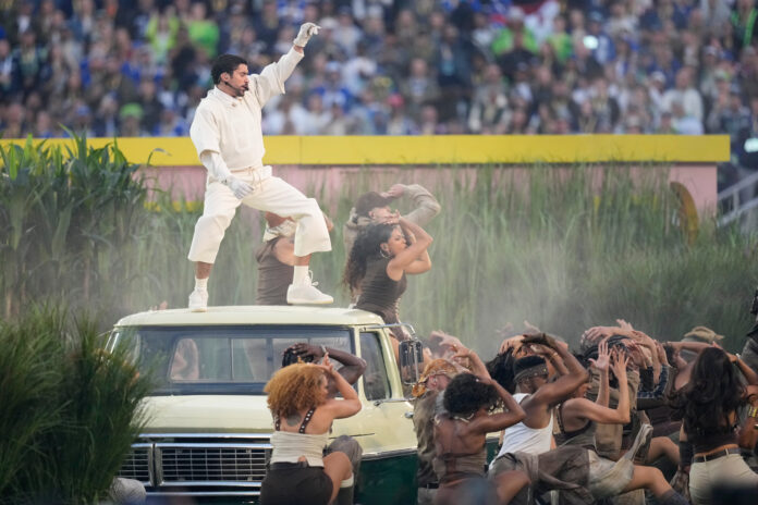 Bad Bunny, vestido de blanco, actúa sobre el techo de un vehículo mientras bailarines participan en el espectáculo de medio tiempo del Super Bowl LX.