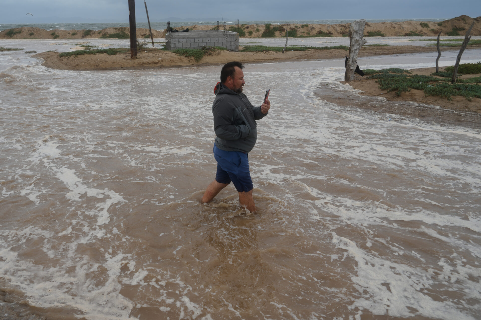 Hombre camina por una calle inundada mientras el agua del mar avanza hacia la costa durante el paso del huracán Polo en Puerto San Carlos, Baja California Sur.