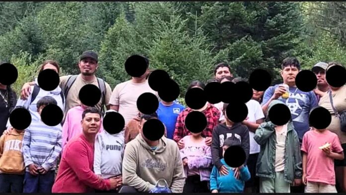 Grupo de adultos y menores posa en un área boscosa durante un viaje familiar de campamento; varios rostros aparecen cubiertos para proteger su identidad.