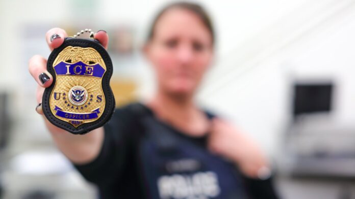 Una agente de U.S. Immigration and Customs Enforcement (ICE) muestra en primer plano una insignia oficial de la agencia.