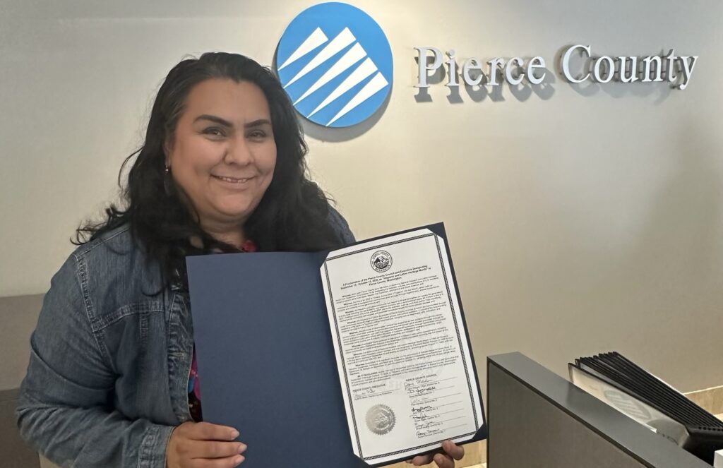 Maribel Galván sostiene la proclamación del Condado de Pierce por el Mes de la Herencia Hispana y Latina frente al letrero de Pierce County.