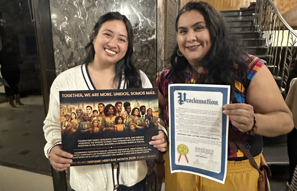 Priscila Desiderio y Maribel Galván posan con material del Mes de la Herencia Hispana y Latina y una proclamación de la Ciudad de Tacoma.