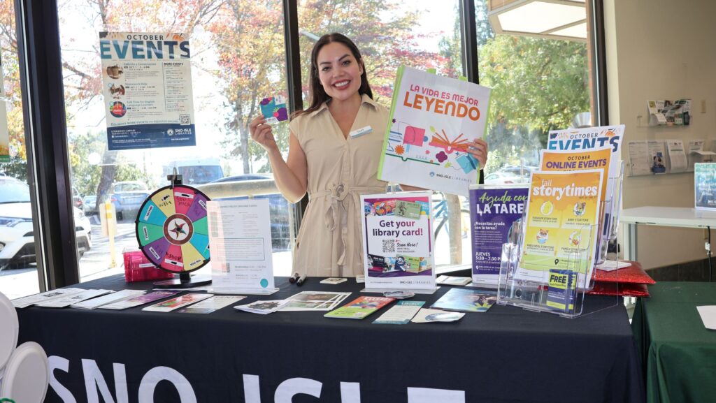 Michelle Cervantes Pérez, Library Associate de Lynnwood Library, muestra una tarjeta de la biblioteca y material informativo en español durante la celebración del Mes de la Herencia Hispana en Lynnwood.