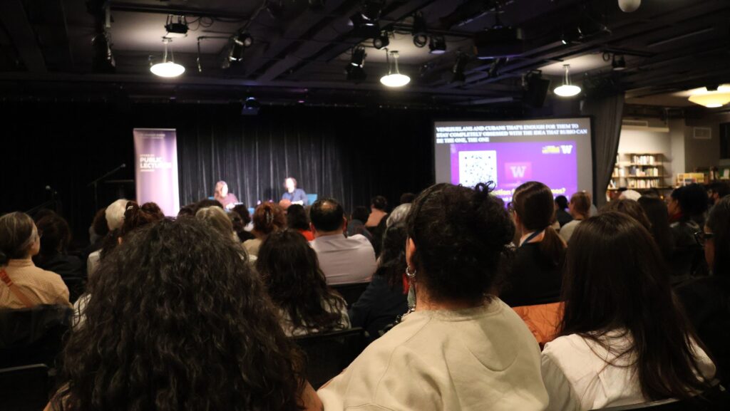 Decenas de asistentes observan desde sus asientos la conversación entre Paola Ramos y Sophia Jordán Wallace en Town Hall Seattle, con una pantalla de la Universidad de Washington al fondo.