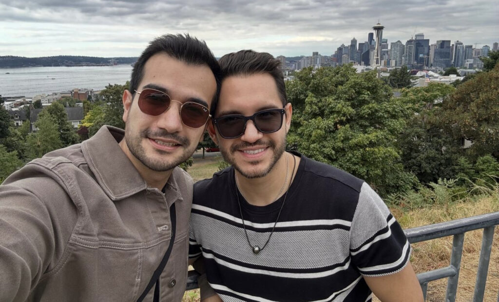 Carlos Iván Ibarra Pacheco y su esposo, Diego González Aspeitia, sonríen mientras se toman una fotografía con la Space Needle y el centro de Seattle al fondo.