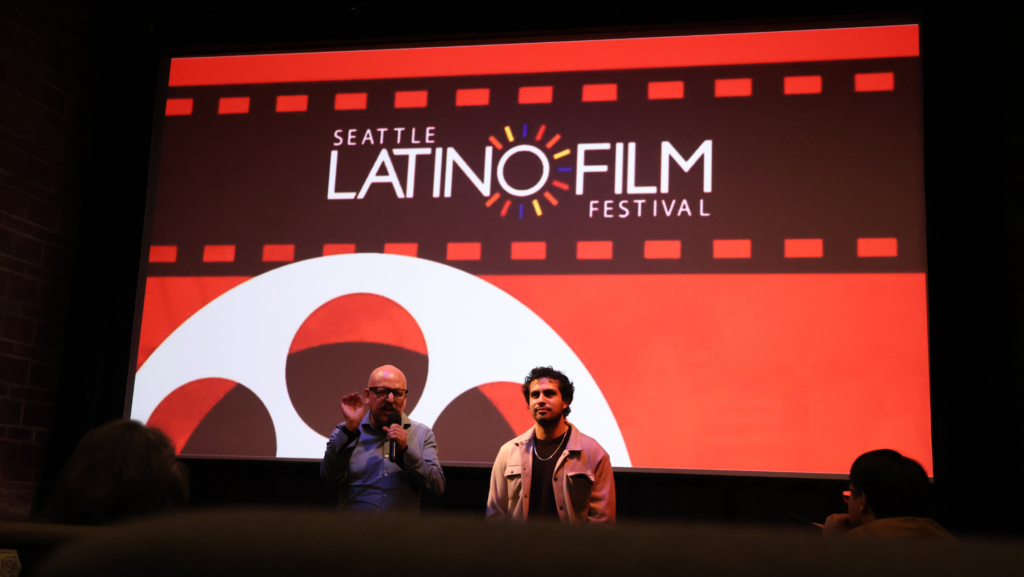 Rafa Lara habla con un micrófono mientras su hijo Rafael Larx permanece a su lado, frente a la pantalla del Seattle Latino Film Festival en el Central Cinema.