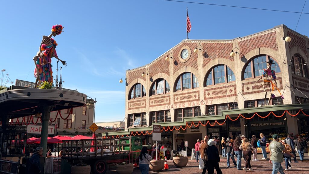 Grandes figuras de esqueletos decoradas con colores vivos adornan los alrededores de Pike Place Market, en Seattle, bajo un cielo despejado.