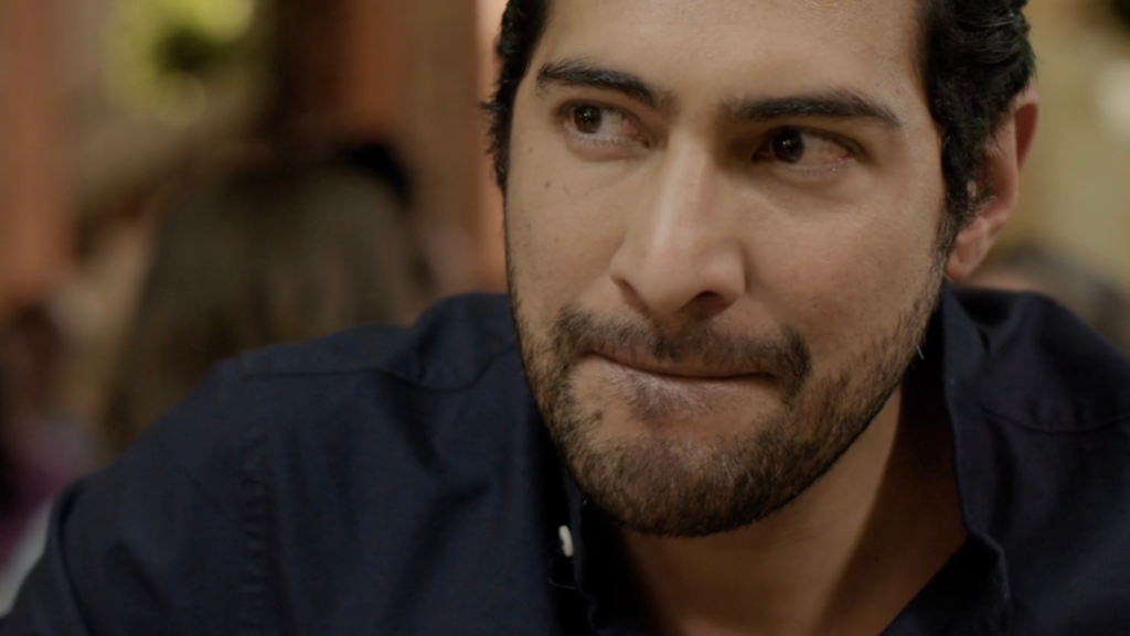 Primer plano del actor mexicano Ianis Guerrero, con barba y camisa azul oscuro, durante una escena de la película “Hijo de familia”.