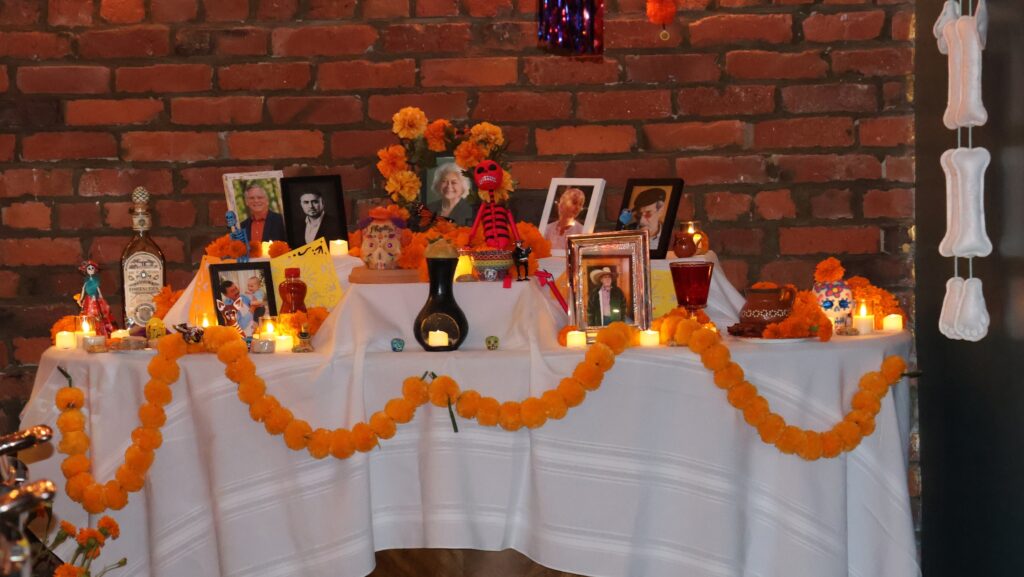 Altar del Día de Muertos instalado en el restaurante Copacabana de Seattle, con fotografías enmarcadas de personas fallecidas, flores de cempasúchil, velas, calaveras decorativas y ofrendas sobre una mesa cubierta con manteles blancos.
