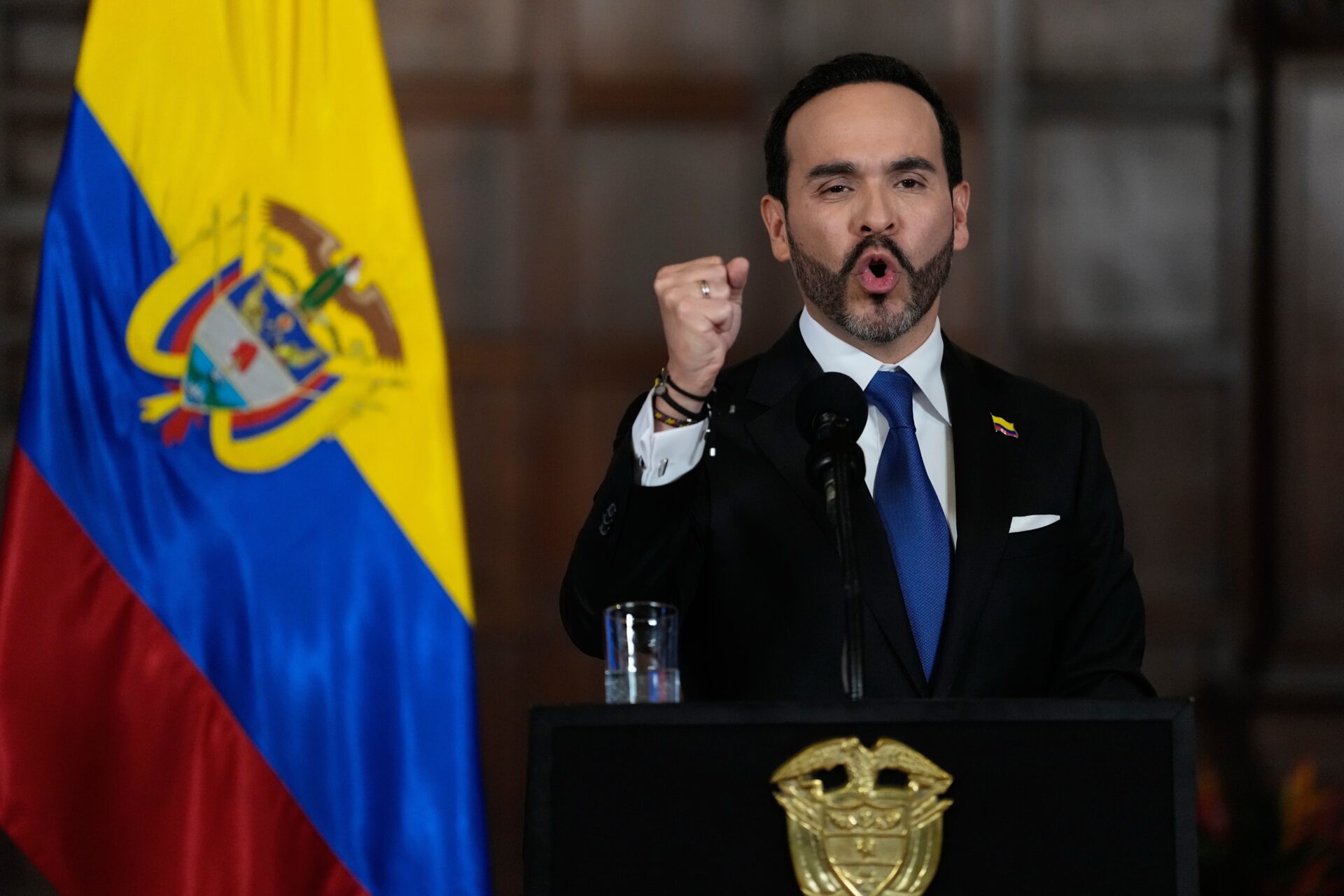 El presidente de Colombia, Abelardo De la Espriella, habla ante un micrófono con el puño derecho levantado durante una declaración oficial en Bogotá. Detrás de él se observa la bandera colombiana.
