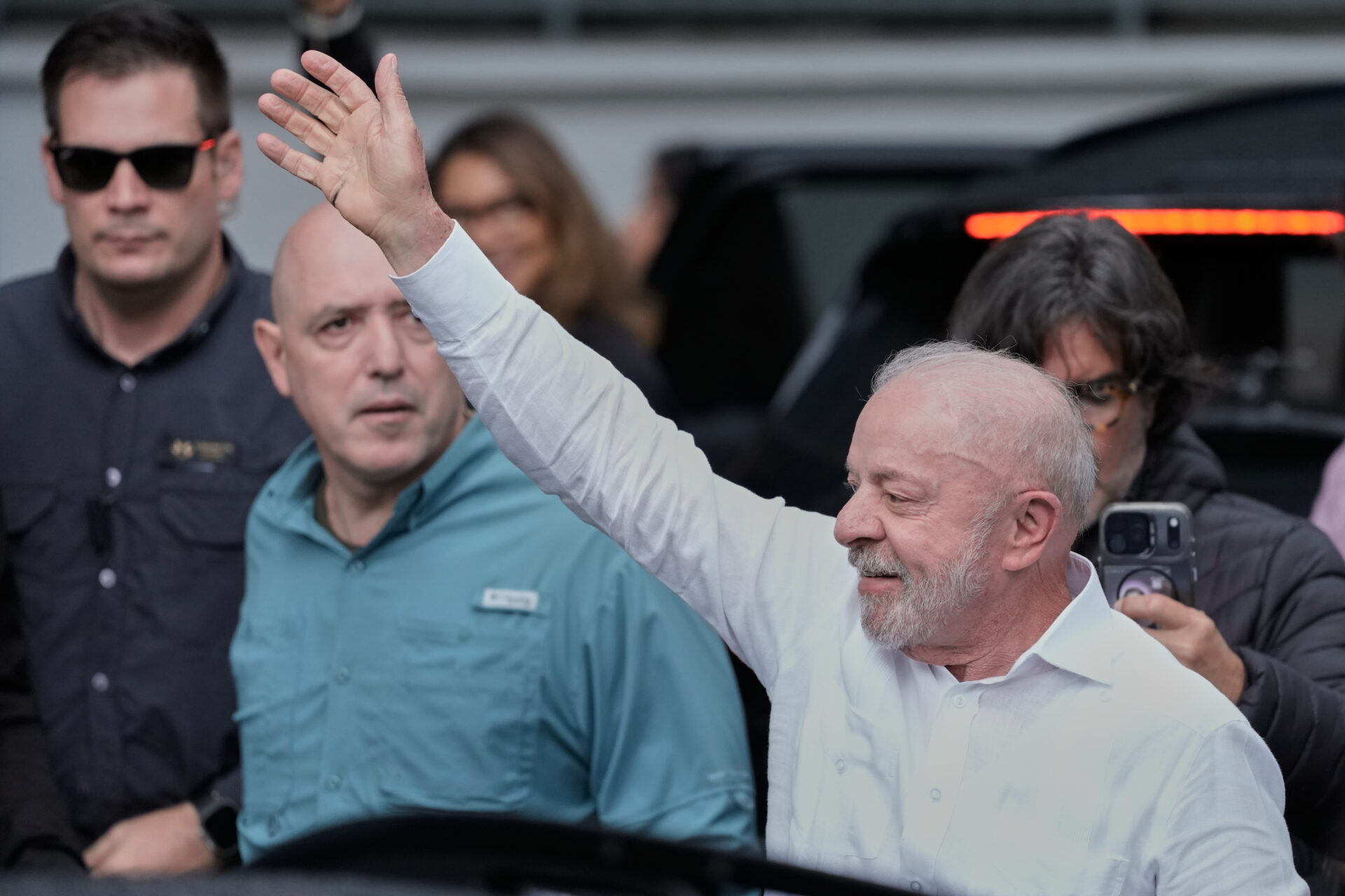 El presidente de Brasil, Luiz Inácio Lula da Silva, saluda con la mano derecha en alto mientras camina rodeado de colaboradores y personal de seguridad.