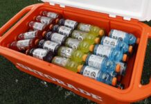 Retiran más de 122,000 cajas de Gatorade vendidas en 37 estados Botellas de Gatorade de varios sabores dentro de una hielera naranja sobre un campo de césped.