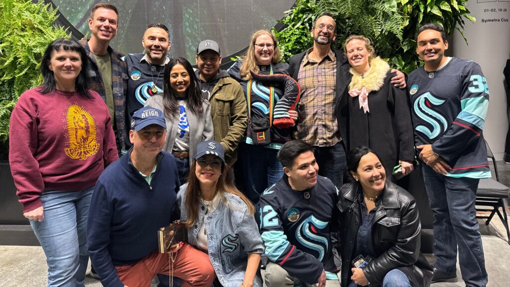 Integrantes del equipo de Entre Hermanos posan juntos, algunos con camisetas de los Seattle Kraken, durante la celebración en el Climate Pledge Arena de Seattle.